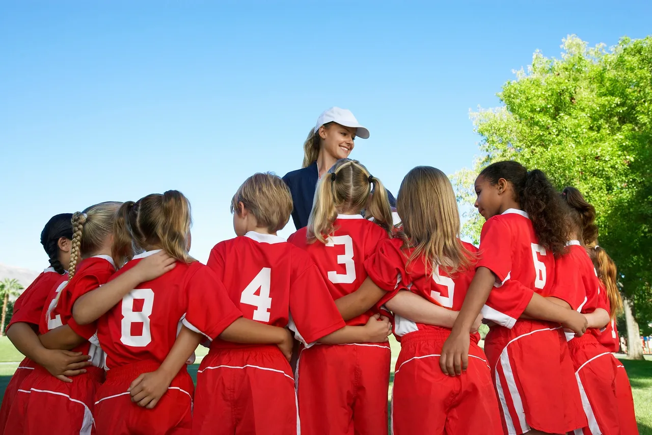 A group of children football players crowd around their female coach