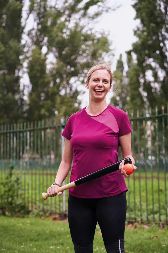 A laughing woman holding a rounders bat and ball