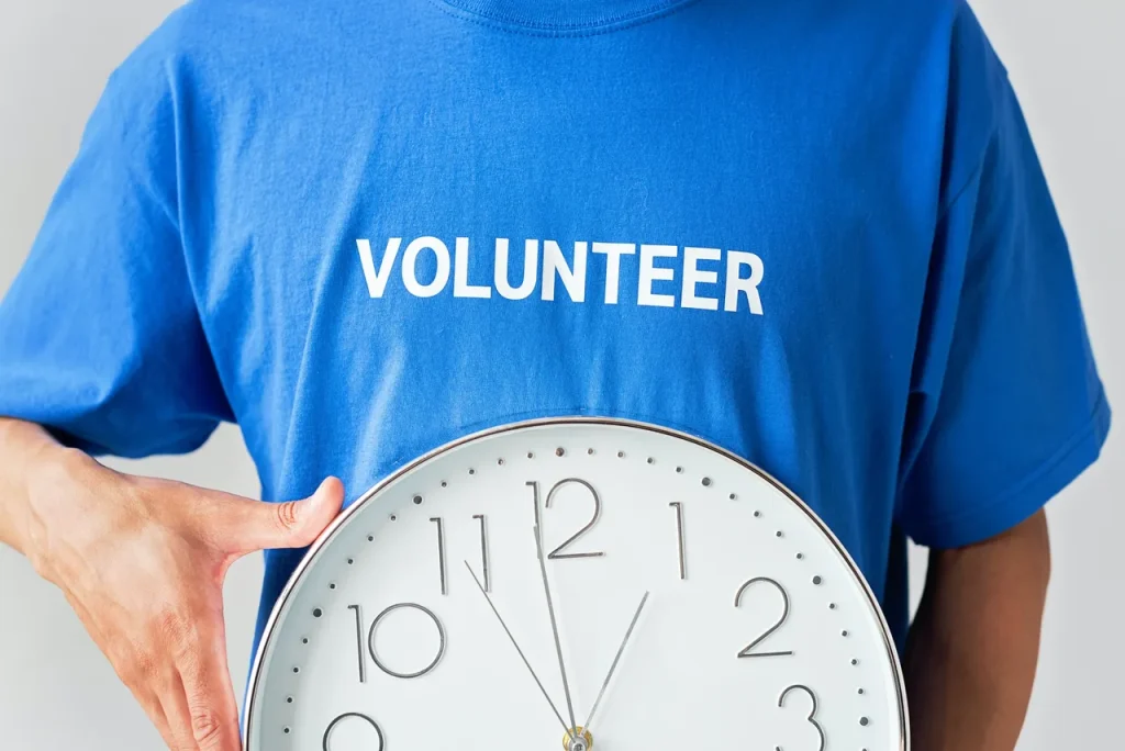 A person with a volunteer t shirt on holding a clock